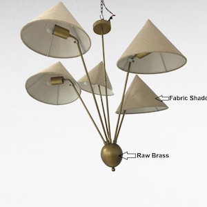 Könnte beinhalten: Ein Kronleuchter im Mid-Century-Modern-Stil mit fünf kegelförmigen Stoffschirmen. Die Leuchte hat eine Rohmessing-Oberfläche und eine zentrale Kugel. Die Schirme sind beige, und die Leuchte ist von der Decke abgehängt.
