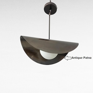 Pode incluir: Luminária pendente moderna com acabamento em bronze escuro. A luminária apresenta uma sombra curva que cobre parcialmente uma luz branca esférica. O texto "Antique Patna" é visível.