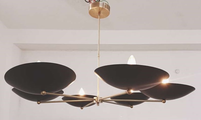 May include: A contemporary chandelier featuring a brass frame and six black, bowl-shaped shades. The light fittings are arranged around a central point, with small light bulbs providing illumination. The chandelier is suspended from the ceiling.