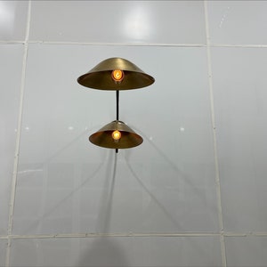 May include: Two gold-toned pendant lights with round shades hang from a white ceiling. The lights are turned on and illuminate the room.