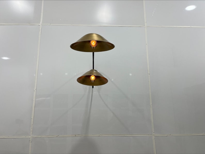 May include: Two gold-toned pendant lights with round shades hang from a white ceiling. The lights are turned on and illuminate the room.