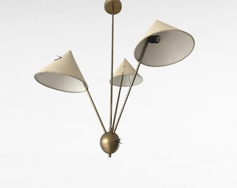 May include: A mid-century modern chandelier with three cone-shaped shades. The shades are a light beige color, and the metal frame has a brass finish. The fixture is designed to be mounted on a ceiling.