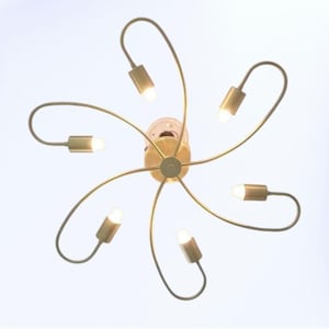 May include: A modern, gold-toned ceiling light fixture with six curved arms, each holding a small, bright light. The fixture is centered and appears against a white background, showcasing a contemporary design.