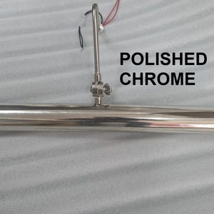 May include: Polished chrome picture light with a cylindrical design. The light has a central mounting fixture and a curved arm. The text "POLISHED CHROME" is displayed in black.