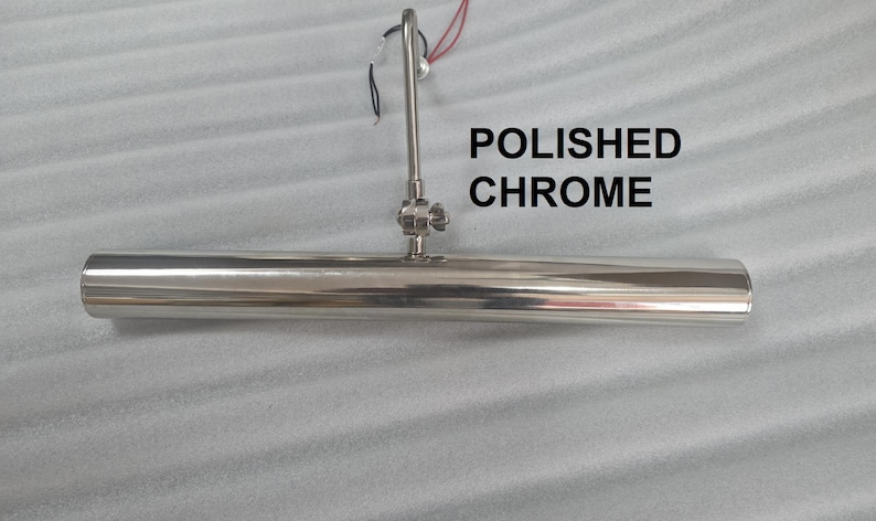 May include: Polished chrome picture light with a cylindrical design. The light has a central mounting fixture and a curved arm. The text "POLISHED CHROME" is displayed in black.
