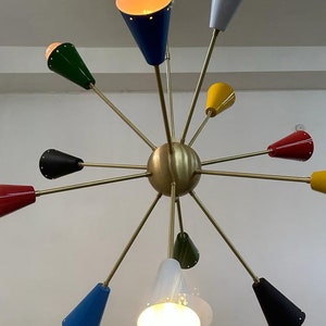 Może przedstawiać: Żyrandol w stylu mid-century modern z mosiężnym wykończeniem i wieloma kloszami w kształcie stożka w r&oacute;żnych kolorach, w tym niebieskim, zielonym, ż&oacute;łtym i czerwonym. Oprawy oświetleniowe są rozmieszczone w wz&oacute;r gwiazdy, z odsłoniętymi żar&oacute;wkami.