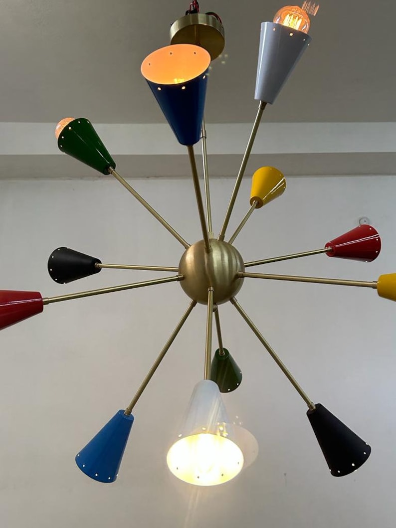 Może przedstawiać: Żyrandol w stylu mid-century modern z mosiężnym wykończeniem i wieloma kloszami w kształcie stożka w r&oacute;żnych kolorach, w tym niebieskim, zielonym, ż&oacute;łtym i czerwonym. Oprawy oświetleniowe są rozmieszczone w wz&oacute;r gwiazdy, z odsłoniętymi żar&oacute;wkami.