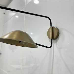 May include: A modern wall sconce with a black metal frame and a gold-toned shade. The sconce has a simple, geometric design and would add a touch of contemporary style to any room.