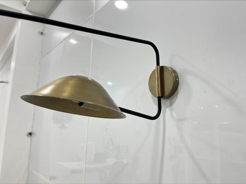 May include: A modern wall sconce with a black metal frame and a gold-toned shade. The sconce has a simple, geometric design and would add a touch of contemporary style to any room.