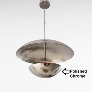 Könnte beinhalten: Pendelleuchte aus poliertem Chrom. Die Leuchte hat ein kreisförmiges Baldachin und zwei schalenförmige Schirme, einer größer als der andere. Die Leuchte hängt an einer schlanken Stange.