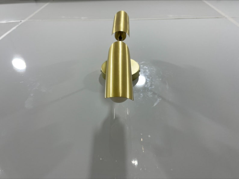 Pode incluir: Uma arandela de parede dourada com duas lumin&aacute;rias. A arandela tem um design simples e moderno.