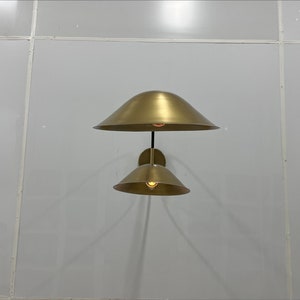 May include: A gold-toned wall sconce with two light fixtures. The sconce has a modern design with two round, bell-shaped shades.