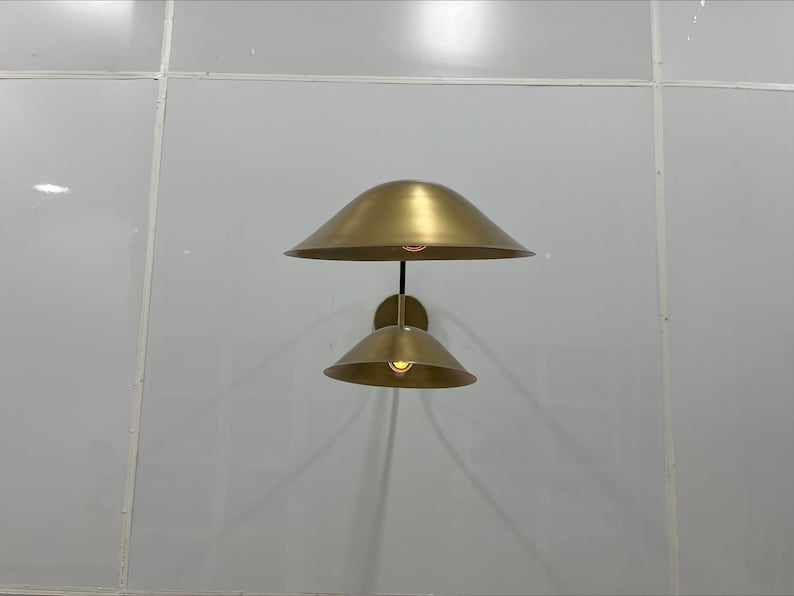 May include: A gold-toned wall sconce with two light fixtures. The sconce has a modern design with two round, bell-shaped shades.