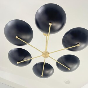 May include: A contemporary ceiling light featuring six black, oval shades. These are connected to gold-toned arms radiating from a central point. The fixture is set against a white ceiling, offering a bold contrast in a room.