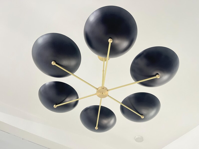 May include: A contemporary ceiling light featuring six black, oval shades. These are connected to gold-toned arms radiating from a central point. The fixture is set against a white ceiling, offering a bold contrast in a room.