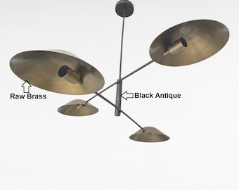 May include: A modern chandelier with four raw brass shades and a black antique frame. The shades are circular and angled, with a cylindrical light fixture in the center. The fixture is suspended from a single point.