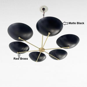 May include: A contemporary matte black chandelier featuring six oval shades. The light fitting has raw brass arms radiating from a central point. It is suspended from a white ceiling fixture, providing a stylish lighting option.