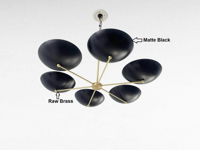 May include: A contemporary matte black chandelier featuring six oval shades. The light fitting has raw brass arms radiating from a central point. It is suspended from a white ceiling fixture, providing a stylish lighting option.