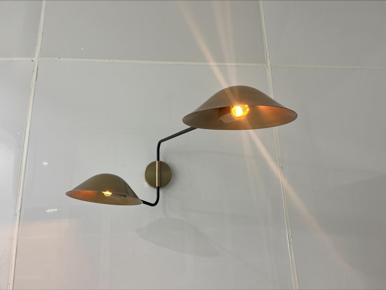 May include: A modern wall sconce with two gold-toned shades and a black metal arm. The shades are angled in opposite directions, creating a unique and stylish look.