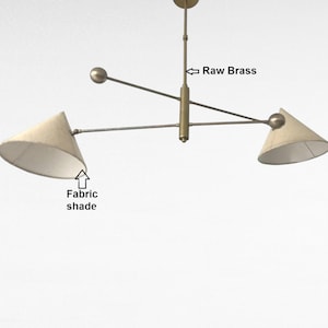 Könnte beinhalten: Eine moderne Deckenleuchte mit Rohmessing-Finish und zwei Stoffschirmen. Die Leuchte hat ein minimalistisches Design mit einer zentralen Stange und horizontalen Armen, die sich zu den Schirmen erstrecken. Die Schirme sind konisch und beige.