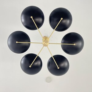May include: A contemporary ceiling light with six black, spherical shades. The shades are attached to a central gold-coloured hub with slender gold arms. The light is mounted on a white ceiling.
