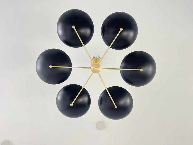 May include: A contemporary ceiling light with six black, spherical shades. The shades are attached to a central gold-coloured hub with slender gold arms. The light is mounted on a white ceiling.