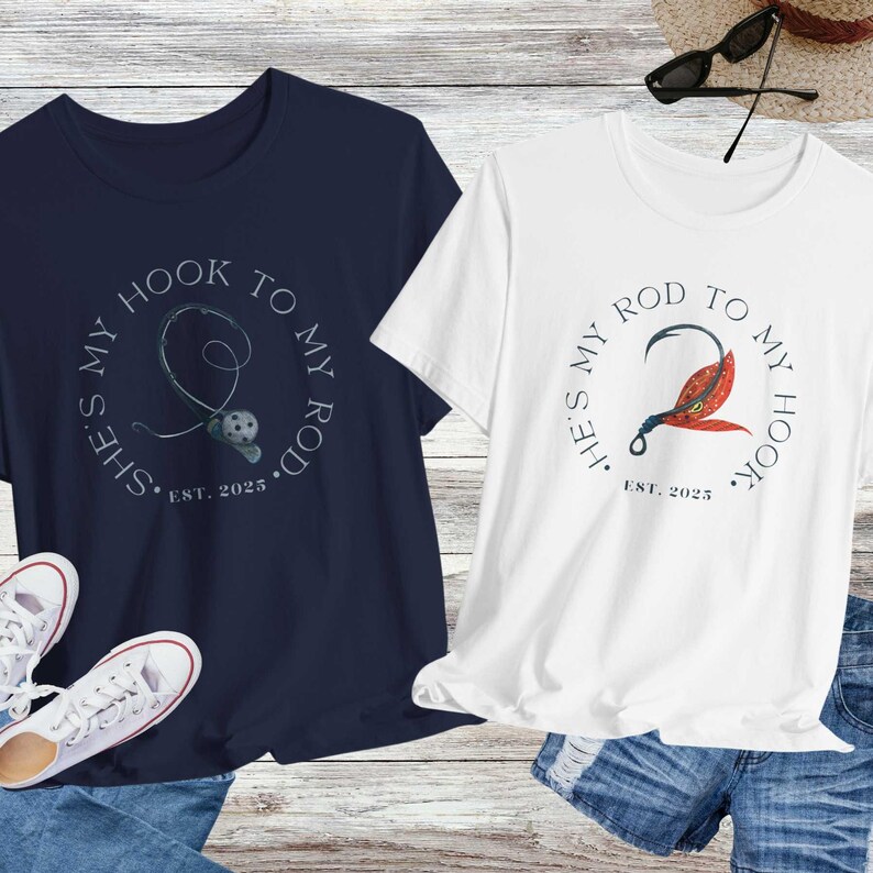 Może przedstawiać: Dwie koszulki z motywem wędkarskim. Niebieska koszulka z napisem "She's my hook to my rod. Est. 2025." Biała koszulka z napisem "He's my rod to my hook. Est. 2025."