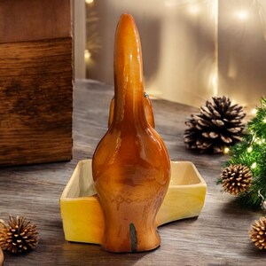 May include: A ceramic dish shaped like a dog, with a brown glazed finish. The dish has a yellow interior and is perfect for holding small items like jewelry or keys.
