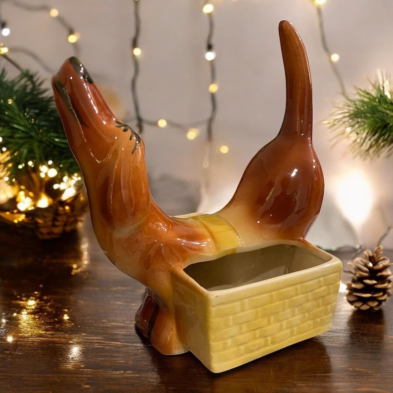 May include: A brown ceramic dachshund planter with a yellow wicker basket inside. The dachshund is standing on its hind legs with its head tilted back and its tail curled up.