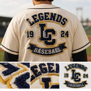 Peut inclure: Un maillot de baseball couleur crème avec des écussons en chenille bleu marine et doré au dos. Le motif comprend le texte LEGENDS, les lettres LC, les chiffres 19 et 24, ainsi qu'une bannière avec le mot BASEBALL en bleu marine et doré.