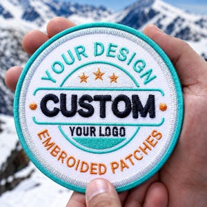 May include: A circular embroidered patch with a white background and a teal border. The text reads YOUR DESIGN in teal, CUSTOM in black, and YOUR LOGO and EMBROIDED PATCHES in orange. Three small orange stars are centered above the word CUSTOM.
