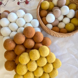 May include: Three sets of felt balls in white, brown, and yellow. The balls are arranged in a circular pattern and are displayed on a white surface.