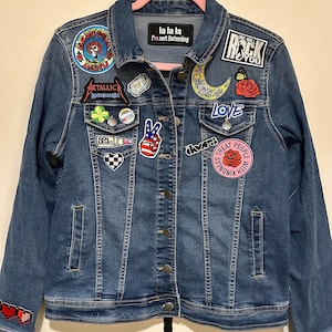 May include: A blue denim jacket with various patches, including a peace sign, a crescent moon, a rose, a heart, a skull, a clover, a lipstick, a checkered pattern, a band logo, and the text "la la la I'm not listening" and "We will rock you".