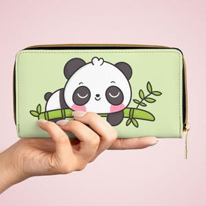 Könnte beinhalten: Ein rechteckiges Portemonnaie mit hellgrünem Hintergrund und einem Cartoon-Panda, der auf einem grünen Bambusstab ruht. Der Panda hat schwarze Ohren, schwarze Augenpartien und rosa Wangen. Das Portemonnaie hat einen schwarzen Reißverschluss.