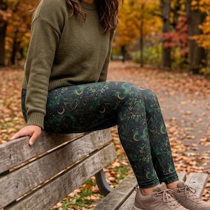 May include: An olive green long-sleeved sweater paired with dark green leggings featuring a celestial print of gold moons and stars. The outfit is completed with beige lace-up athletic sneakers with thick soles and a textured tread pattern.