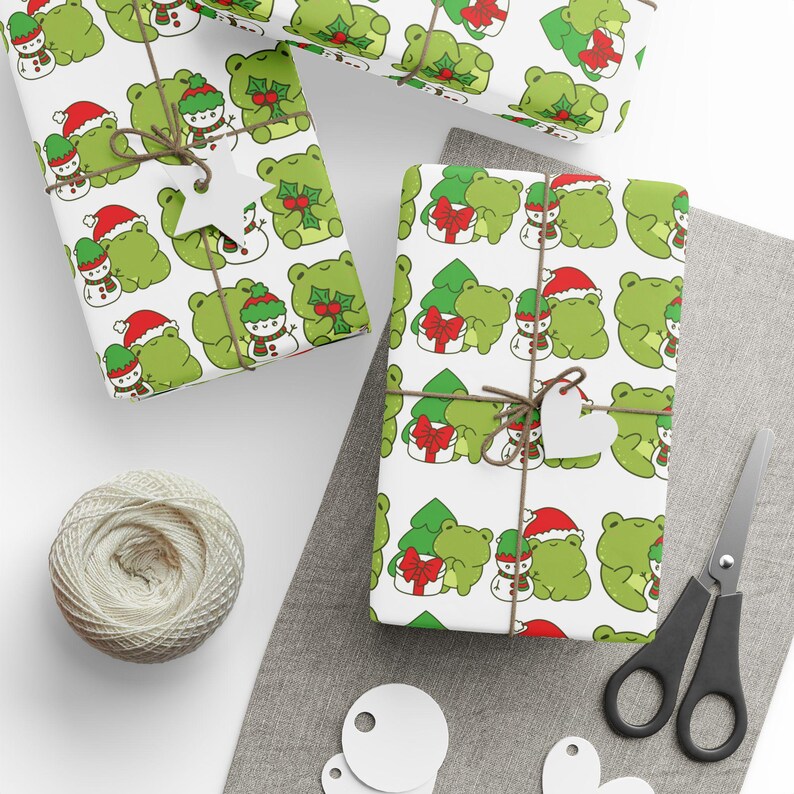 May include: White wrapping paper with a repeating pattern of green frogs wearing Santa hats and holding small snowmen. The frogs are surrounded by green Christmas trees with red bows.