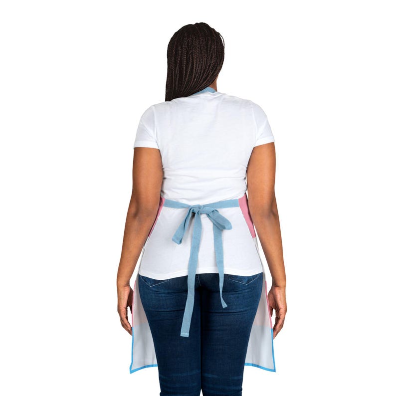 May include: A white t-shirt and dark blue jeans worn with an apron featuring horizontal stripes in light blue, pink, and white. The apron is secured at the waist with a light blue fabric tie, showcasing a clean, functional design for daily tasks.