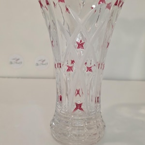 May include: Clear glass vase with a flared top and a patterned design. The vase features a series of red star-shaped accents throughout its body. The vase is designed for decorative purposes.