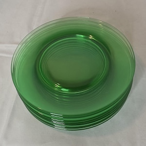 May include: A stack of green glass plates. Each plate has a circular, ridged design on the inside. The plates are a vibrant, transparent green color. The plates are likely for serving food.