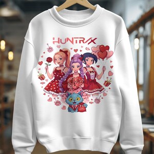 Puede incluir: Sudadera blanca con el texto "HUNTRAX" y un gráfico colorido. El gráfico representa a tres mujeres de estilo anime con vestidos rojos que sostienen regalos, rosas y globos. También aparece un gato azul con un regalo en forma de corazón.