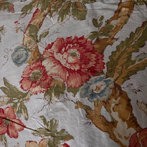 May include: A white fabric featuring a repeating botanical pattern with large red and orange peonies, smaller blue flowers, and green leaves. The design includes brown tree-like branches winding through the floral arrangement on the textile.