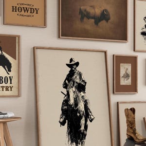 May include: A collection of framed art prints with a Western theme. The prints feature images of cowboys, rodeo scenes, a bison, and the word "HOWDY". The frames are a warm brown color, and the art has a vintage aesthetic.