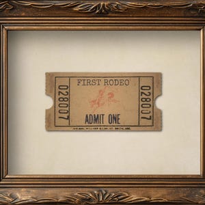 May include: A framed vintage rodeo ticket with the text "FIRST RODEO" and "ADMIT ONE". The ticket is tan with brown text and a graphic of a rodeo rider. The frame is ornate, brown, and rectangular.