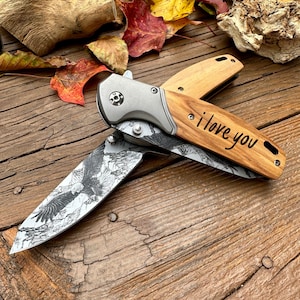 May include: A pocket knife with a wooden handle engraved with the words "i love you". The blade is decorated with a black and white image of an eagle.