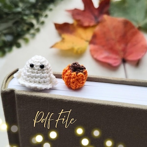 Puede incluir: Un fantasma blanco tejido a ganchillo y una calabaza naranja tejida a ganchillo están sobre un libro. El fantasma tiene dos ojos negros. La calabaza tiene un tallo marrón. El texto "Pdf File" está escrito en cursiva en el libro.