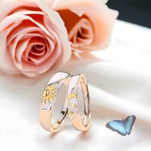 Könnte beinhalten: Zwei goldene Eheringe mit einem weißen Emaille-Design. Ein Ring zeigt eine Sonne, der andere einen Mond.