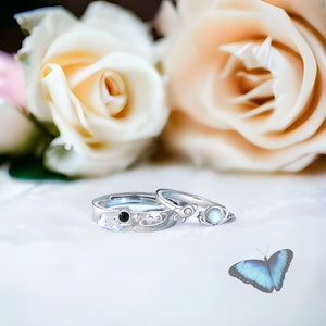 Puede incluir: Dos anillos de plata con un detalle de piedra negra y blanca. Los anillos están sobre una superficie blanca con una mariposa azul.