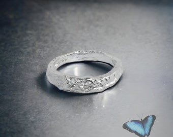May include: A silver ring with a textured surface and two small clear stones. The ring is on a gray background.