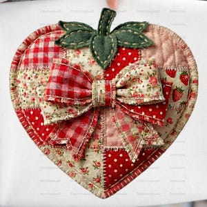 Könnte beinhalten: Ein weißes Stoffobjekt mit einem herzförmigen Erdbeermotiv. Die Erdbeere besteht aus Patchwork-Stoff in Rot, Weiß und Grün, mit einer Schleife und grünen Blättern. Das Design umfasst rote Punkte, Vichy-Karo und Blumenmuster.