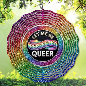 May include: A rainbow-colored, glittery wind spinner with the text "LET ME BE PERFECTLY QUEER" in a circular design. The spinner is suspended from a chain and features a wavy, layered design with a vibrant spectrum of colors.